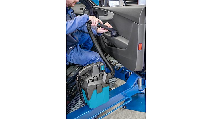 Eine Person reinigt den Innenraum eines Autos mit dem 9543-10 Akku-Staubsauger. Der blaue Staubsauger ist tragbar und wird mit einem Schlauch verwendet. Der Hintergrund zeigt das ge&ouml;ffnete Autot&uuml;rinnere.