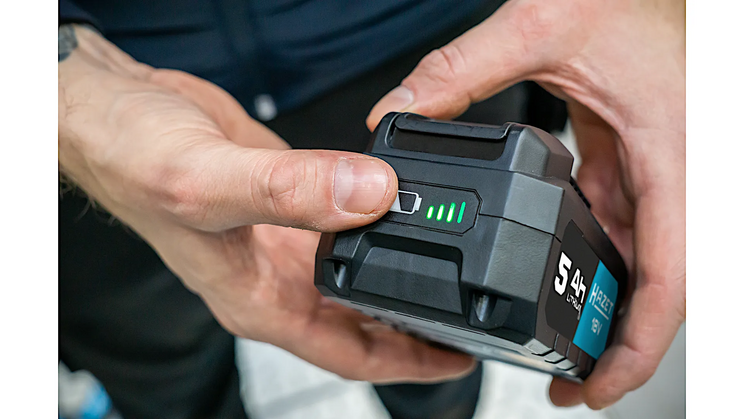 Eine Person dr&uuml;ckt auf den Ladestatus-Knopf eines schwarzen 18V-Akkus mit blauer Beschriftung, um den Ladezustand an der LED-Anzeige zu pr&uuml;fen.